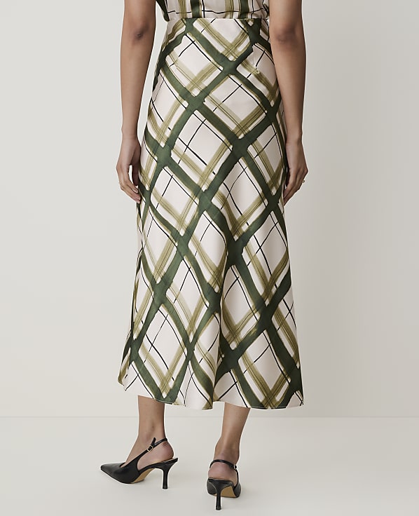 A person wearing a cream-colored skirt with a green diamond pattern and black heels stands against a plain white background.