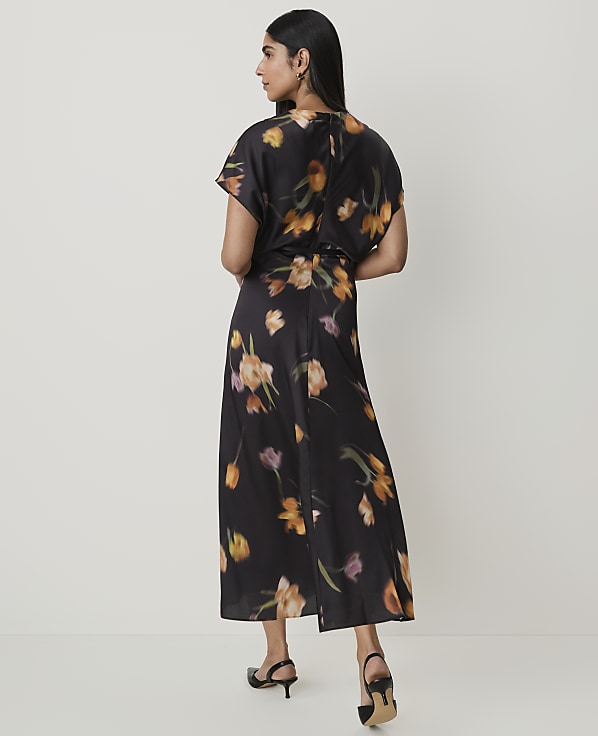 A woman in a black floral dress stands against a plain white background.