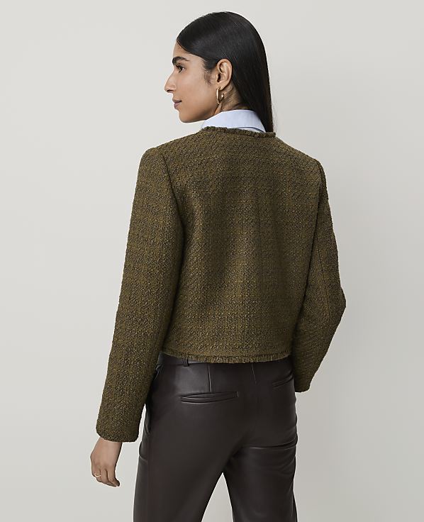 A woman in a textured green jacket and brown leather pants stands against a plain, light-colored background.