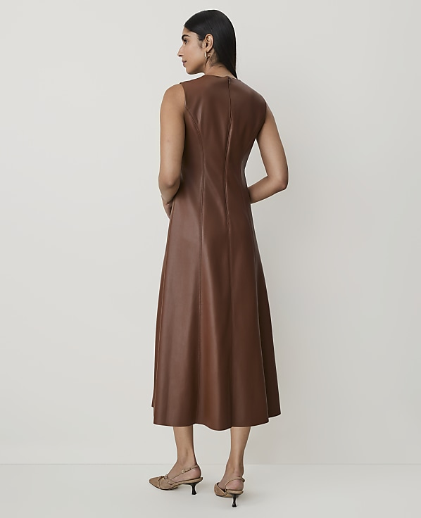 A woman in a brown faux leather dress stands against a plain, light-colored background.
