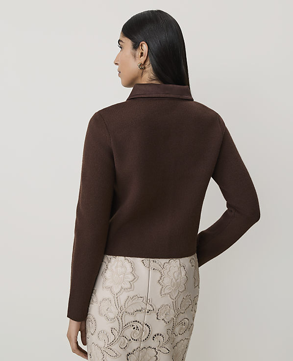 A woman in a brown jacket and a patterned skirt stands against a plain background.