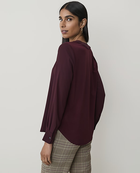 A woman in a burgundy blouse and plaid pants poses against a plain, light-colored background.