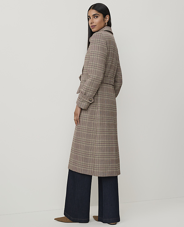 A woman in a plaid coat and wide-leg jeans stands against a plain background.