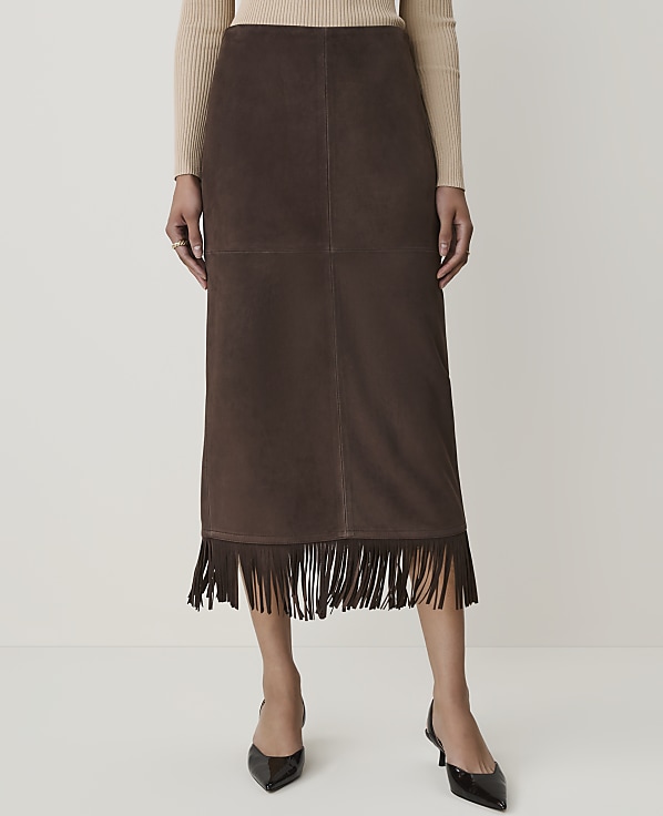 A person models a brown suede skirt with fringe detailing in the foreground, against a plain white background.