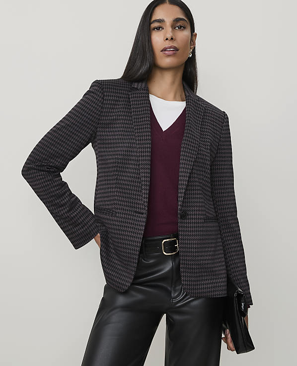 A woman in a patterned blazer and leather pants poses against a plain background.