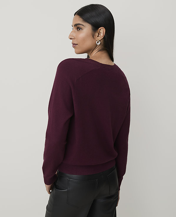 A woman in a burgundy sweater and black leather pants stands against a plain, light gray background.