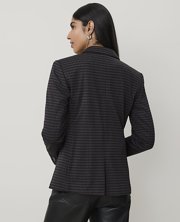 A woman in a houndstooth blazer and leather pants stands against a plain, light-colored background.