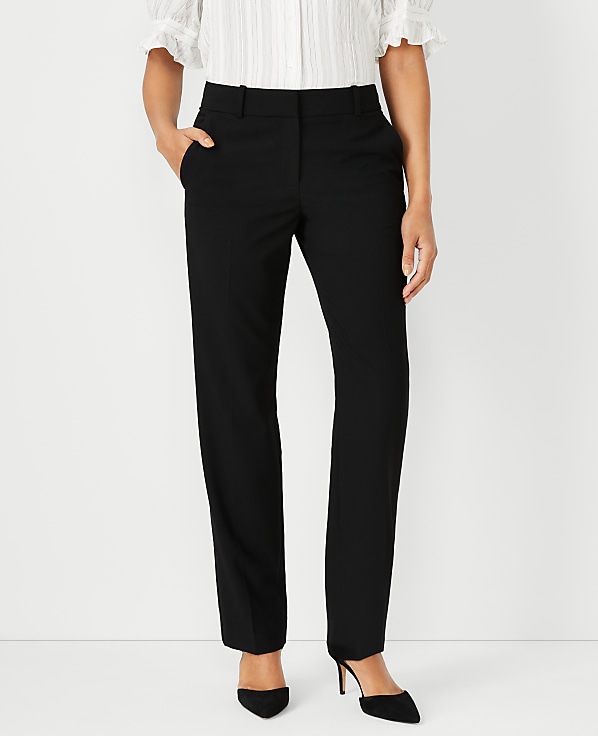 A person in black pants and a white blouse stands against a plain white background.