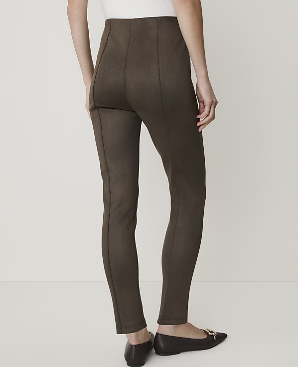 A person wearing brown leggings and brown flats stands against a plain white background.