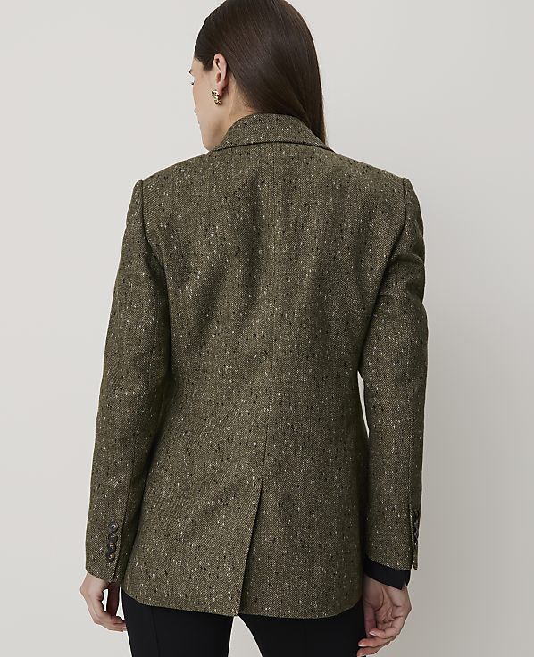 A woman in a textured green blazer stands against a plain, light-colored background.