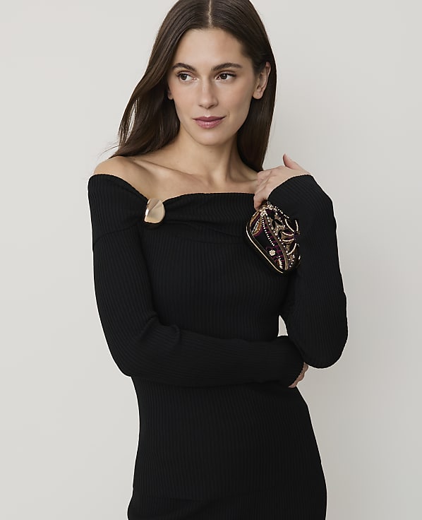A woman in a black off-the-shoulder dress holds a jeweled clutch in the foreground against a plain, light background.