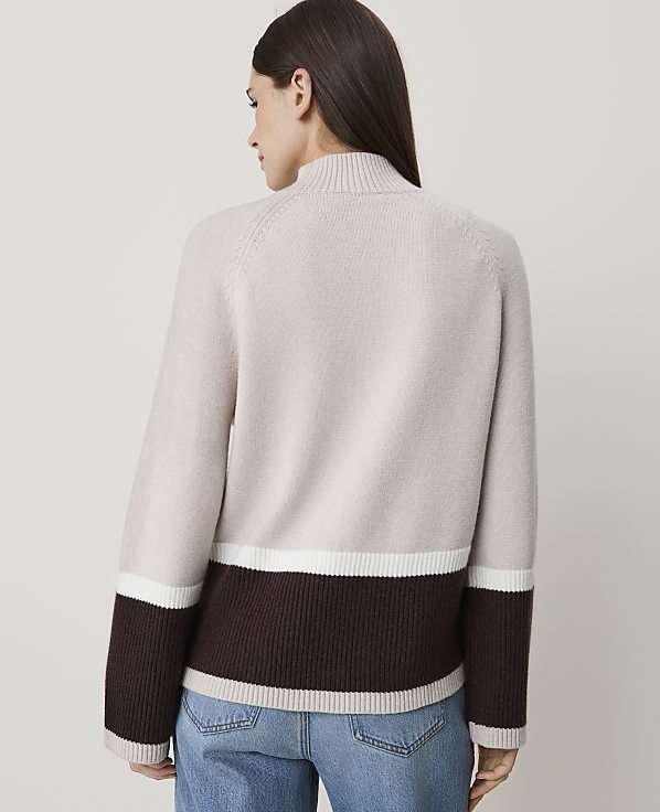 A woman in a color-blocked sweater stands against a plain, light background.