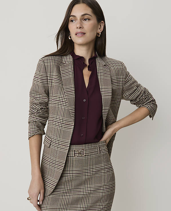 A woman in a plaid suit stands against a plain, light-colored background.