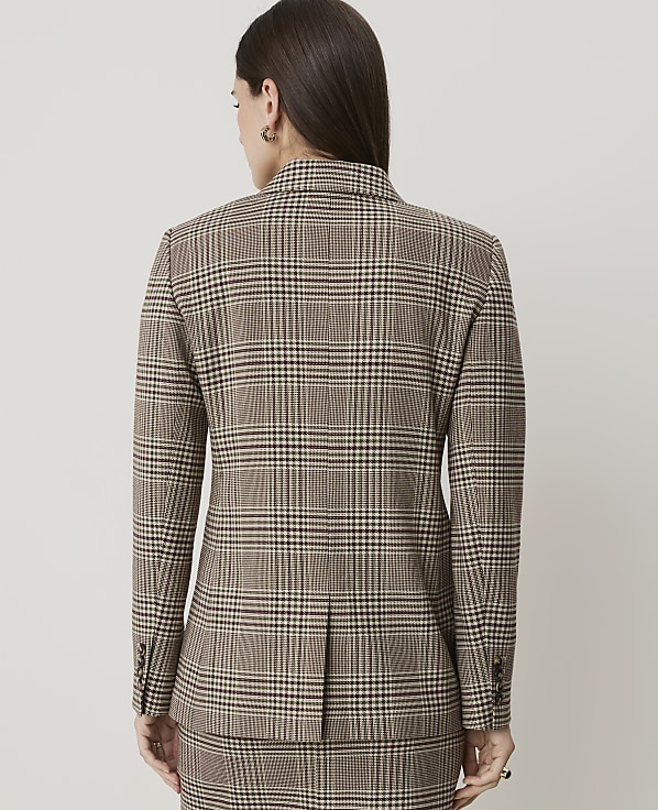 A woman in a brown plaid blazer and skirt stands against a plain, light gray background.