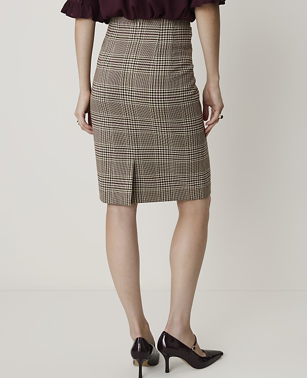 A woman in a plaid pencil skirt and heels stands against a plain white background.