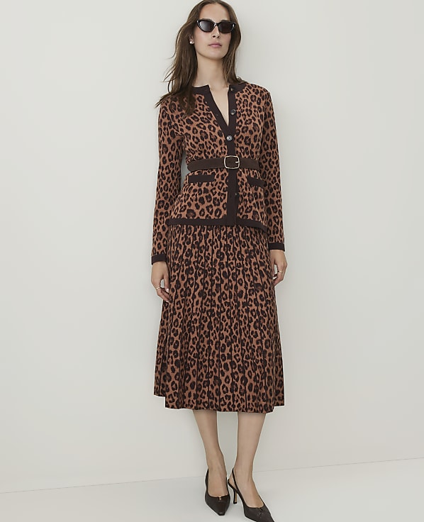 A woman in a leopard-print cardigan and skirt stands against a plain, light-colored background.