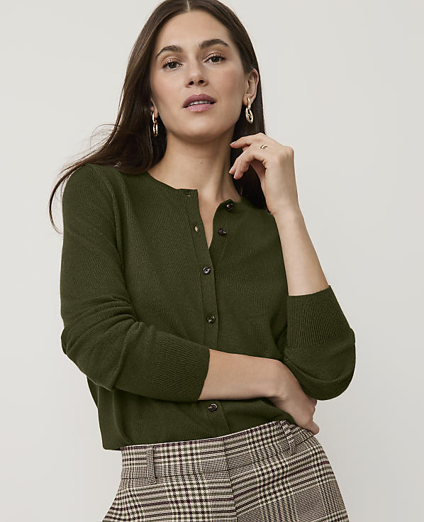 A woman in a brown cardigan and plaid pants poses against a plain background.