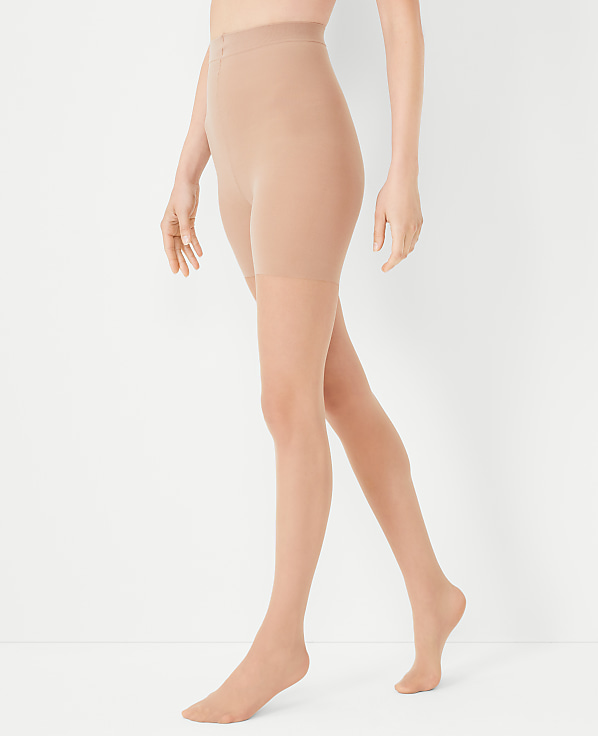 A person's legs are shown from the waist down, wearing sheer nude pantyhose against a plain white background.