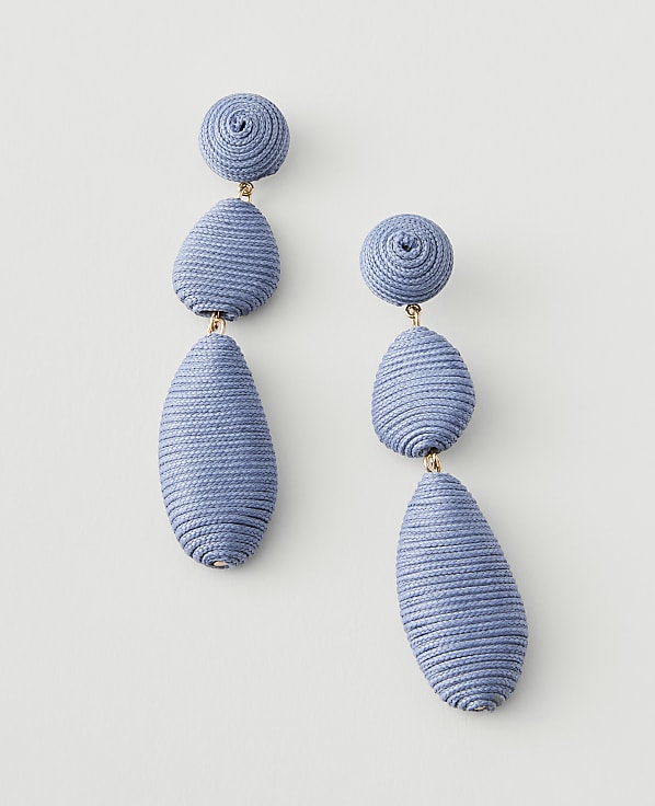 A pair of light blue, textured drop earrings with round and irregular shapes hang against a plain white background.