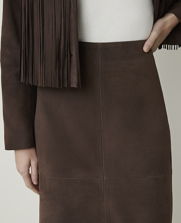 A close-up of a brown suede skirt and fringed jacket is shown against a plain background.