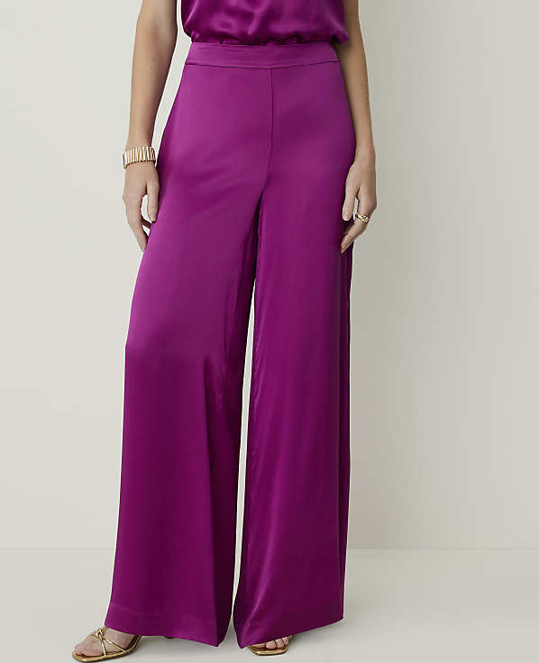 A person wearing wide-leg magenta satin pants and gold sandals stands against a plain, light-colored background.