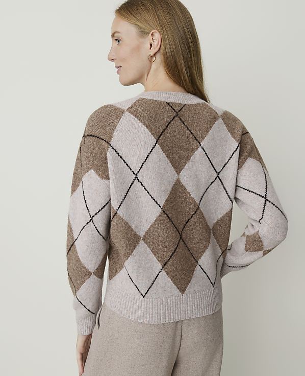 A woman in a tan argyle sweater stands against a plain, light-colored background.