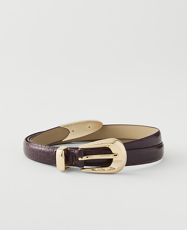 A dark purple, textured belt with a gold buckle lies on a plain white background.