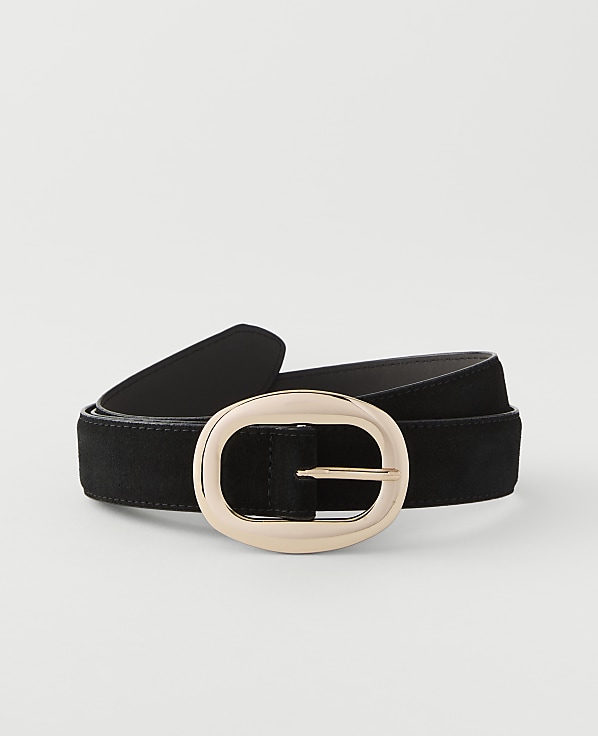 A black suede belt with a large, oval, rose gold buckle rests on a plain white background.
