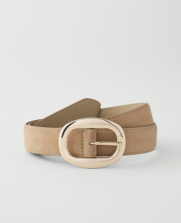 A tan suede belt with a large, oval, rose gold buckle lies on a plain white background.