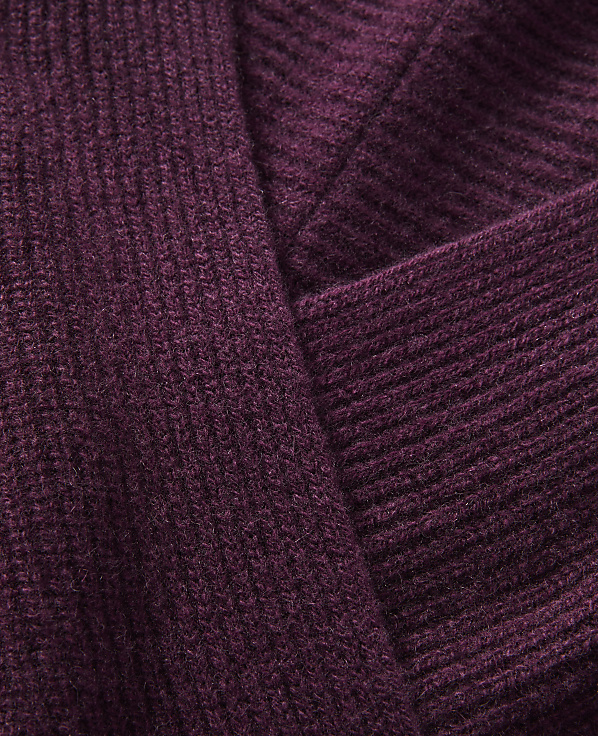 A close-up view of a ribbed, plum-colored knit fabric folds over itself, creating a textured background.