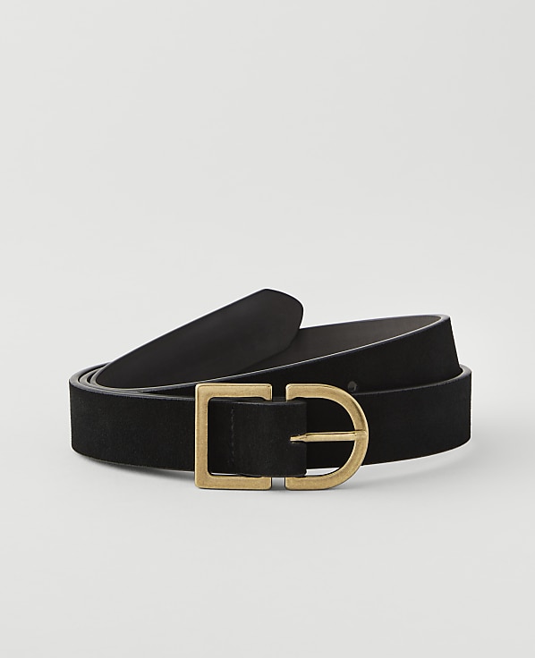 A black suede belt with a brass buckle lies coiled on a plain white background.