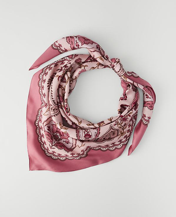 A pink paisley patterned silk scarf is tied in a knot against a plain white background.