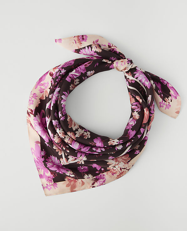 A floral patterned silk scarf with pink and purple flowers is tied in a knot against a plain white background.