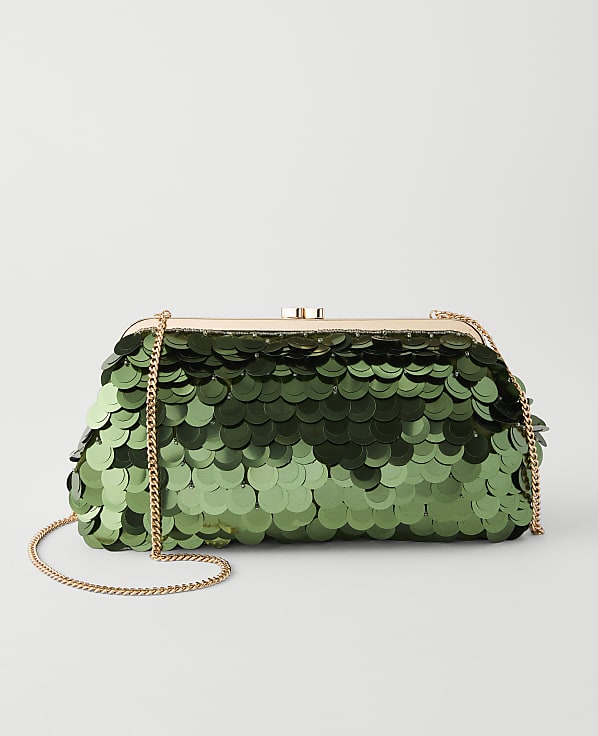 A green sequined clutch with a gold chain rests against a plain, light gray background.