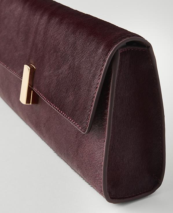 A burgundy clutch with a gold clasp rests on a white surface.