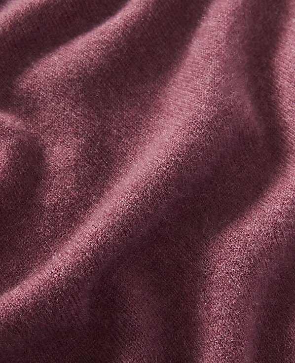 A close-up of a textured, rose-colored fabric with soft folds fills the frame, with no discernible background.