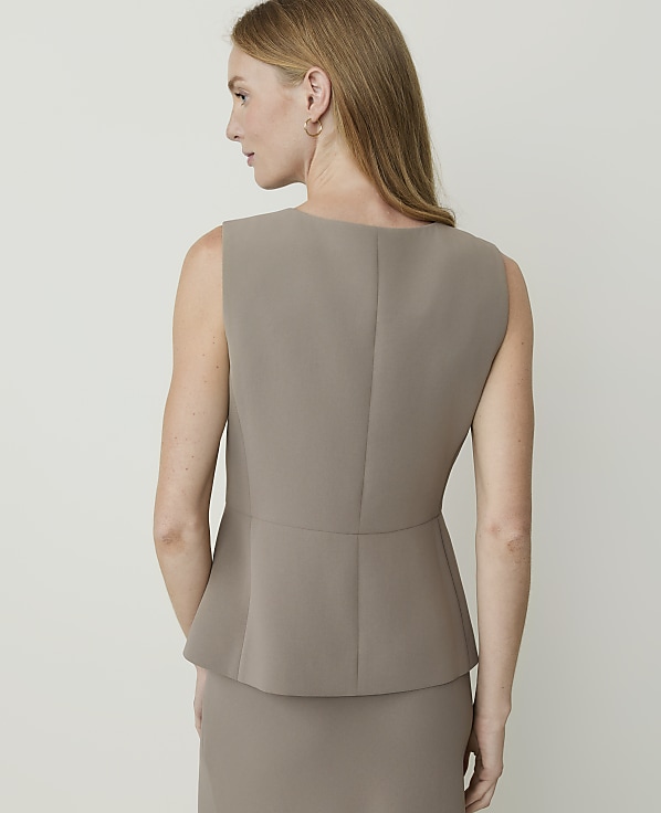 A woman in a taupe peplum top and skirt stands against a plain, light background.