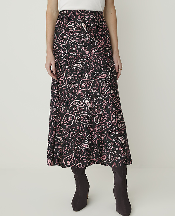 A woman in a black and pink paisley skirt and dark boots stands against a plain white background.