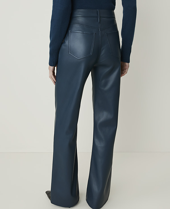A person wearing teal faux leather flared pants stands against a plain, light-colored background.