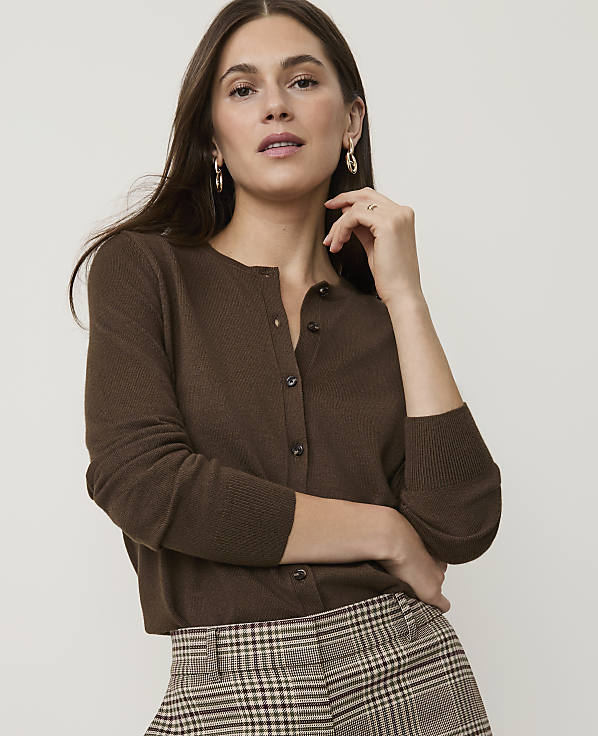 A woman in a brown cardigan and plaid pants poses against a plain background.