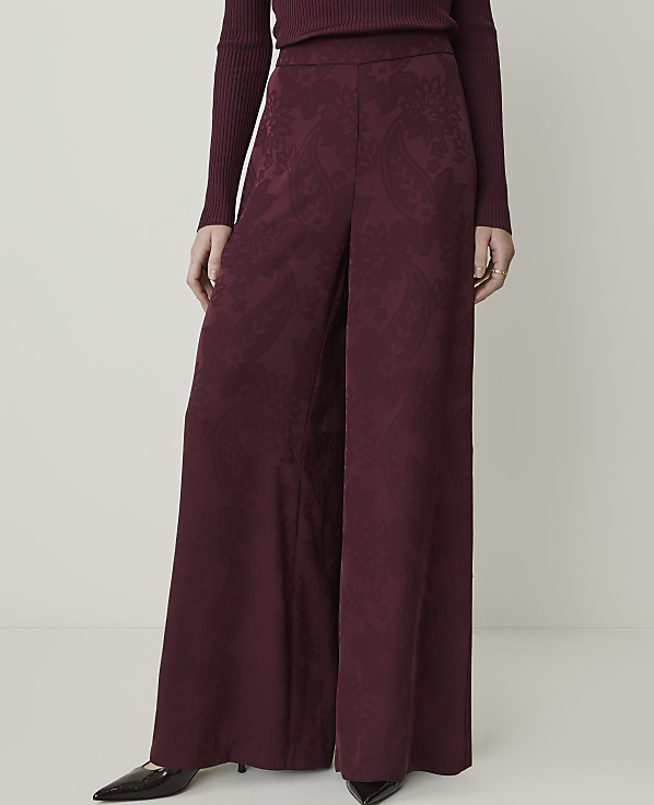 A person stands in wide-leg burgundy patterned pants and a ribbed sweater against a plain white background.