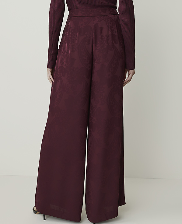 A person stands in wide-leg burgundy pants with a paisley pattern in the foreground, against a plain white background.