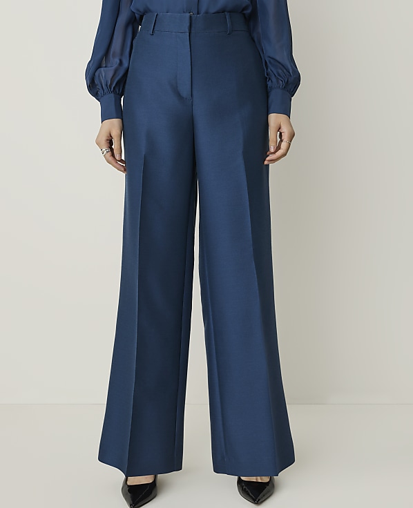 A person stands in wide-leg teal trousers and black pointed-toe heels against a plain white background.