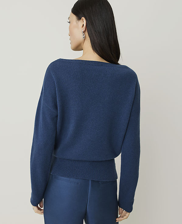 A woman in a blue sweater and pants stands against a plain, light gray background.