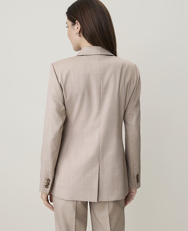 A woman in a beige plaid suit stands against a plain, light-colored background.