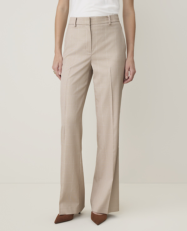 A person in beige pinstripe flared trousers and brown pointed-toe heels stands against a plain, light-colored background.