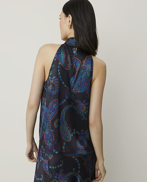 A woman in a dark, paisley-patterned halter top stands against a plain, light background.