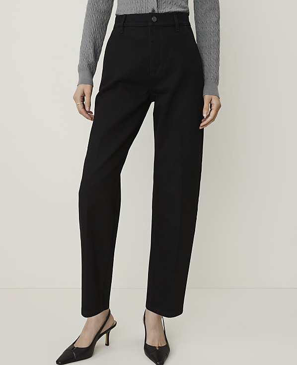 A person in black pants and a grey sweater stands against a plain white background.
