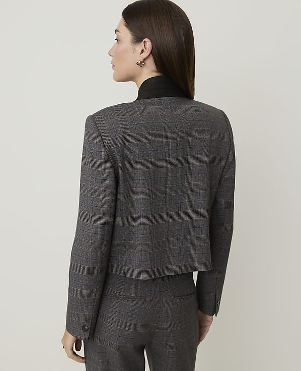 A woman in a plaid suit stands against a plain, light-colored background.
