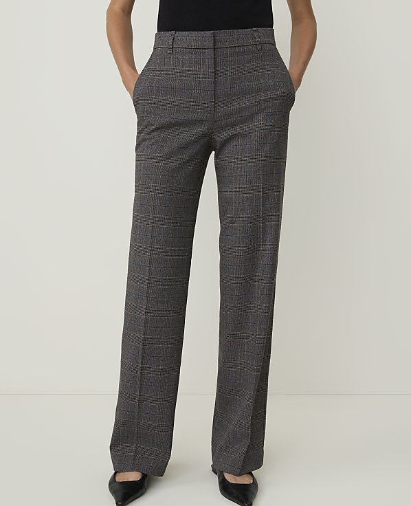 A person stands in front of a plain white background, wearing plaid trousers and black pointed-toe shoes.